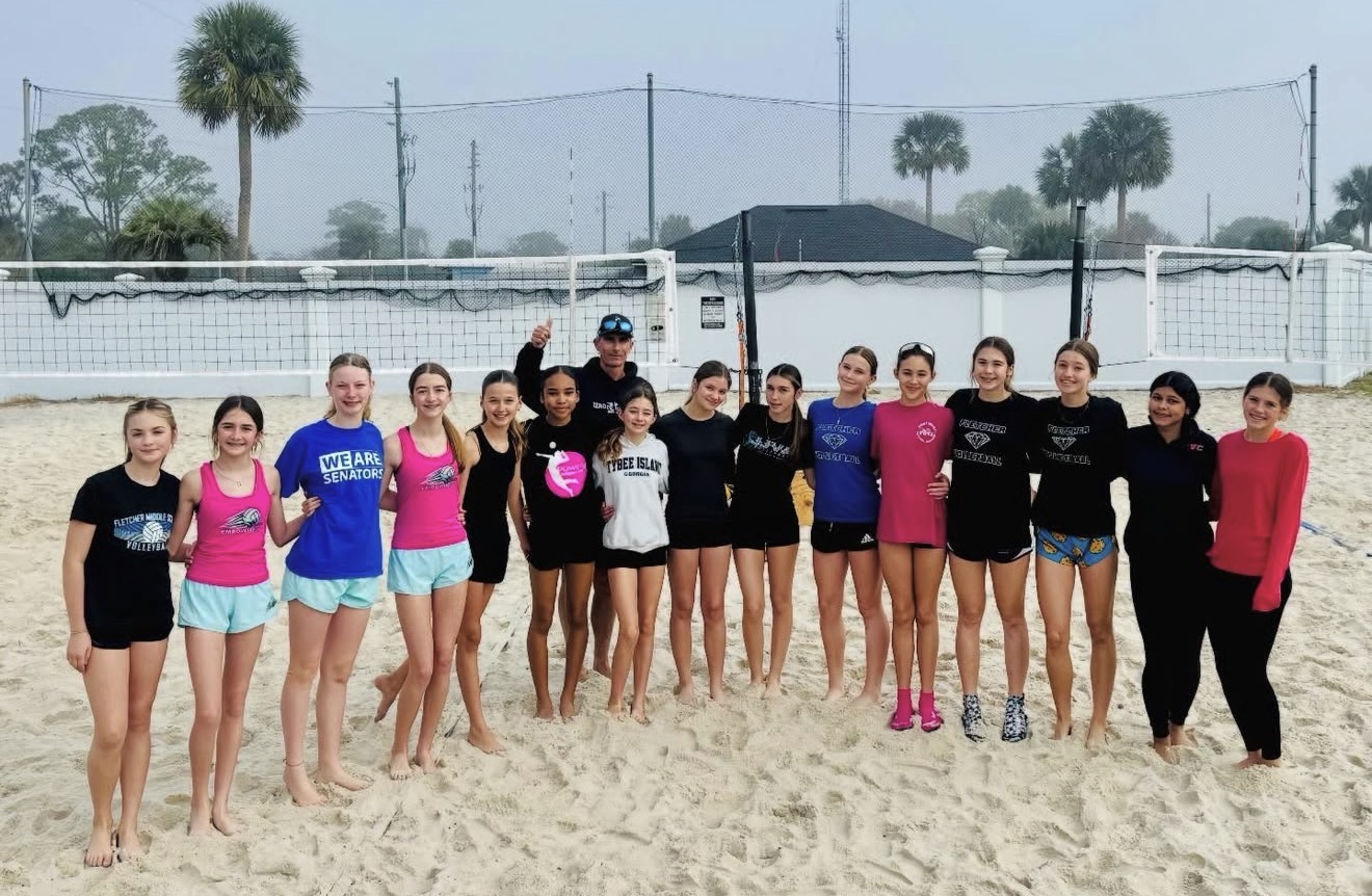 A group of people stands on a beach, wearing sports attire and smiling for a photo.