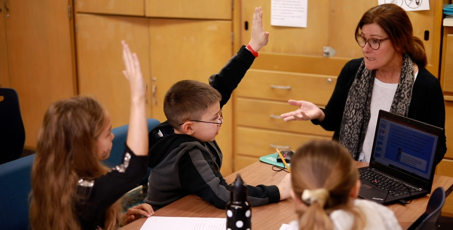 Students raising hands in classroom with laptop open