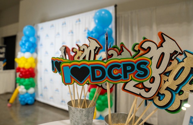 A table with a sign that reads "I love DCPS" in colorful letters. Colorful balloons and a backdrop are in the background.