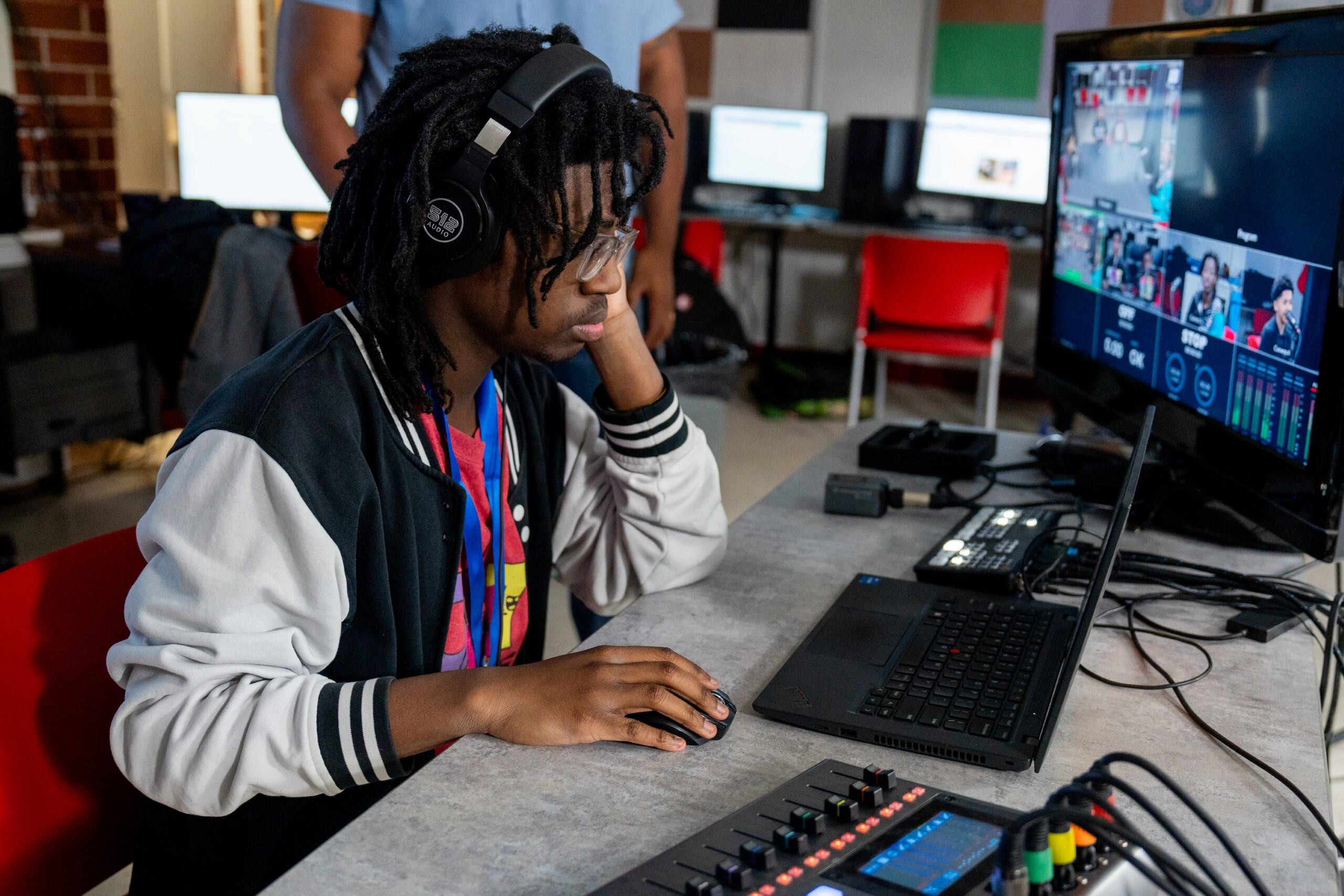 A student with headphones working on a switch board and directing a podcast