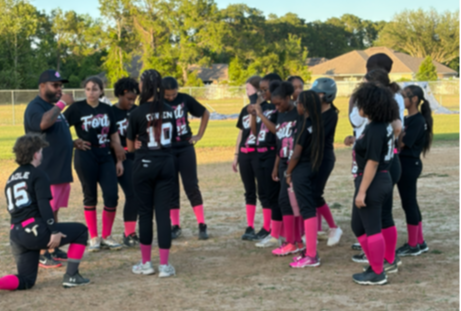 A group of young athletes in black uniforms and pink socks are gathered on a field.