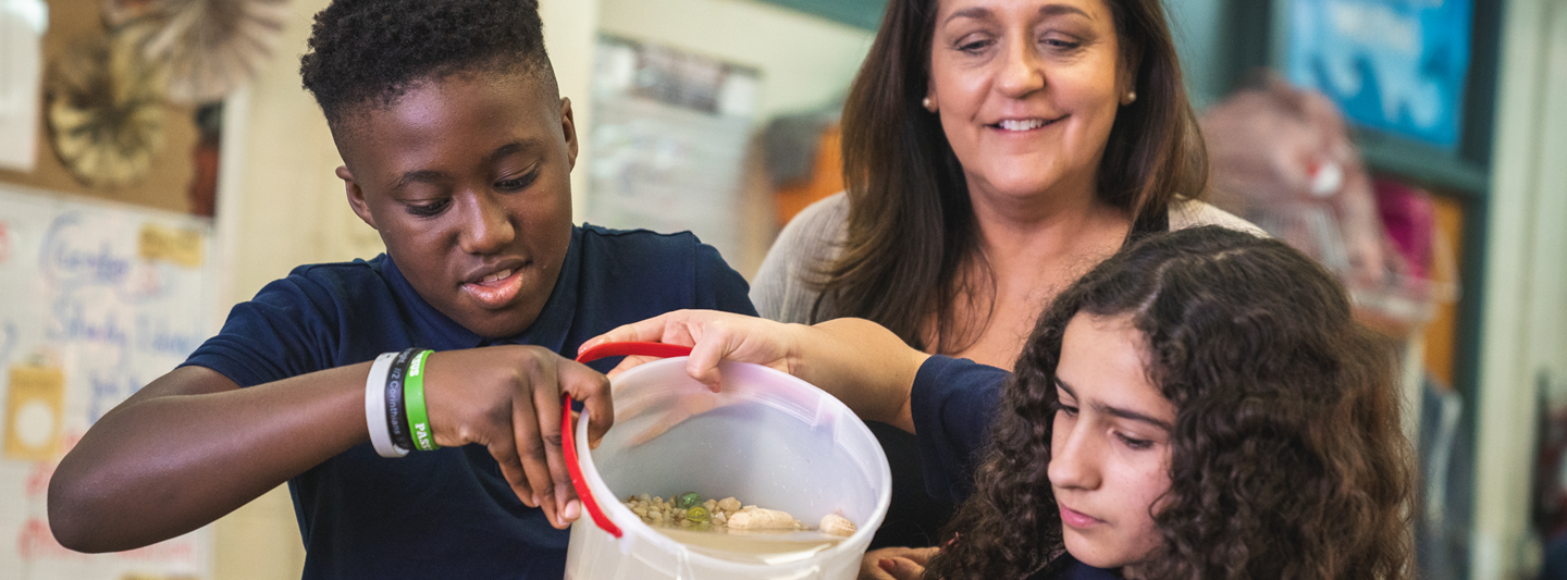 teacher and two students working on a science project with a bucket of water and rocks