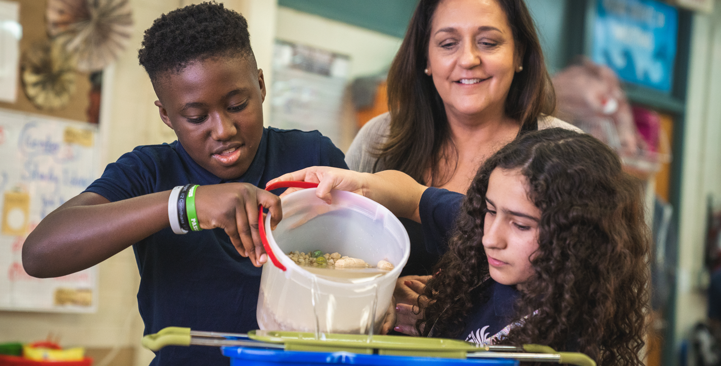 teacher and two students working on a science project with a bucket of water and rocks