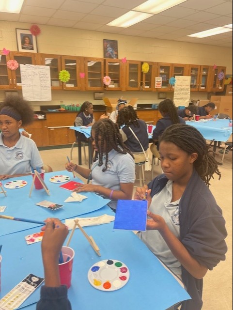 Several students are seated around a table, engaging in a painting activity in a classroom.