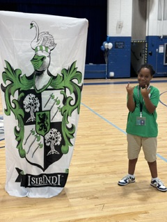 A banner with a green coat of arms is standing on a wooden floor. A child stands beside it.