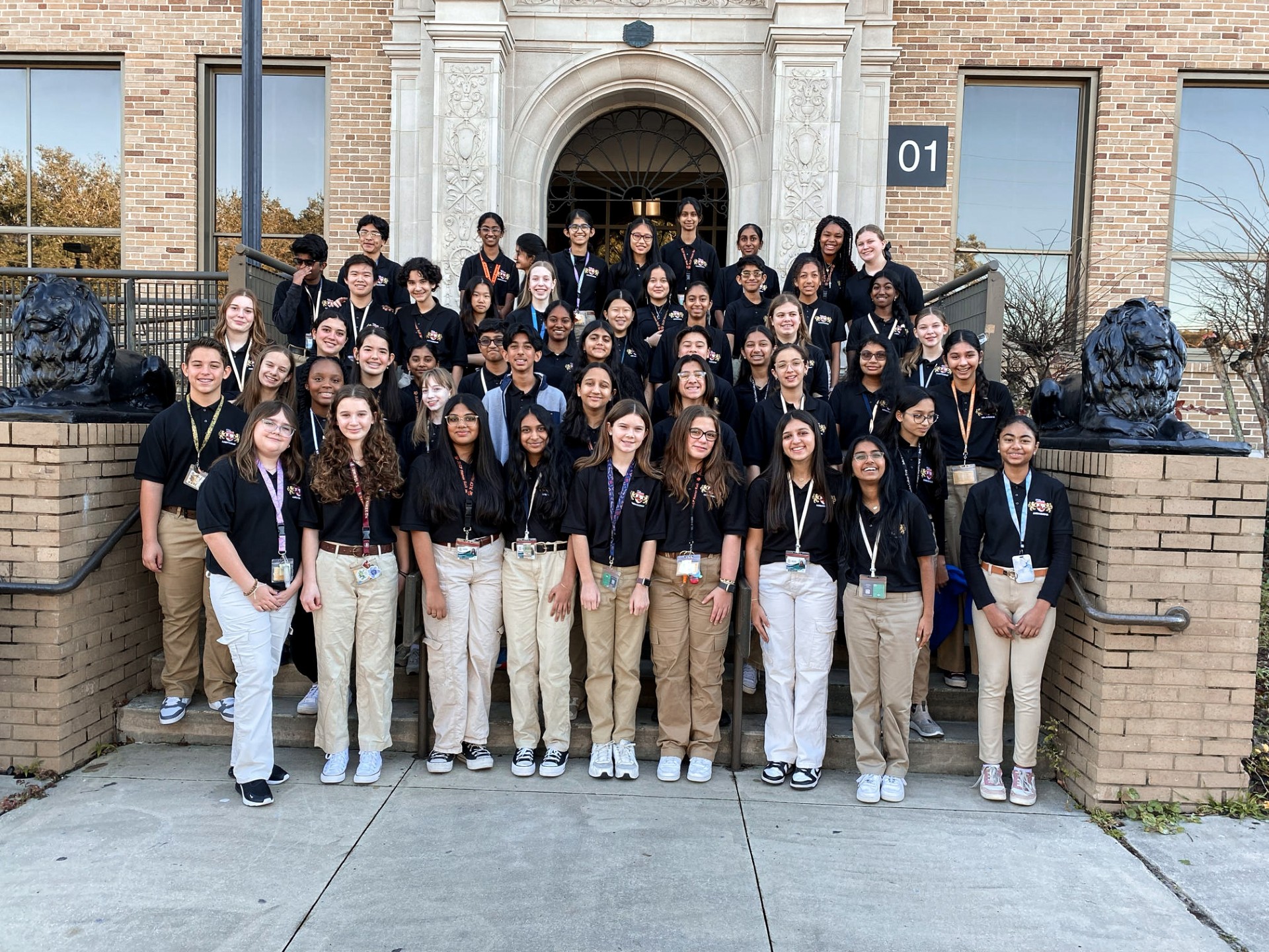 A group of students in matching shirts and pants poses for a photo in front of a building.