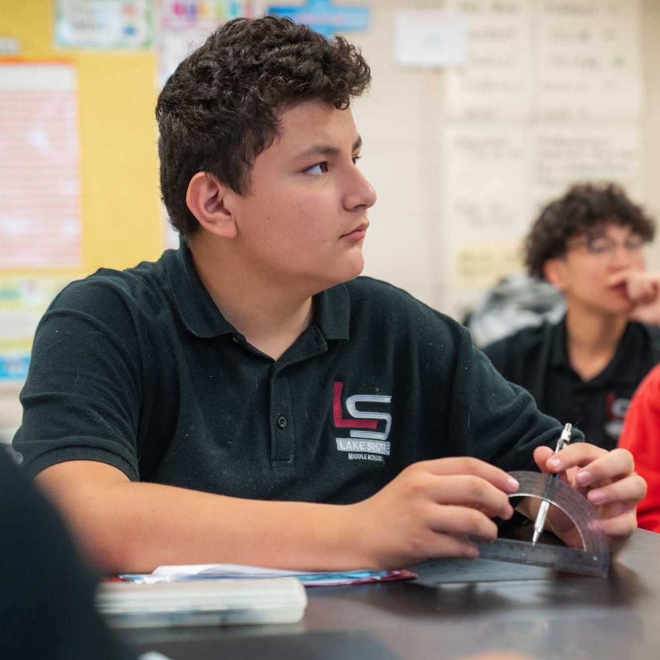 Student paying attention in class at their desk with a pencil and measuring tool.