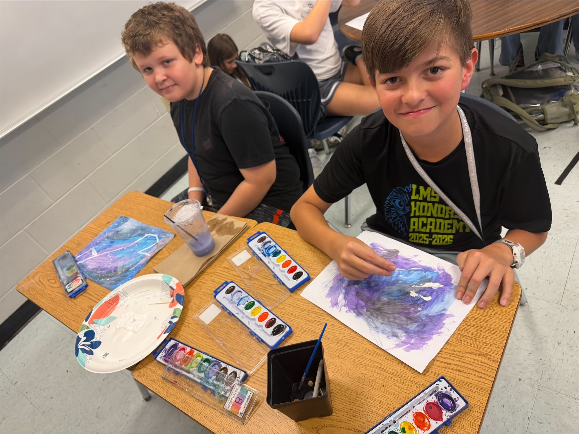 Two male students in black tshirts creating watercolors in shades of blue, purple and black.