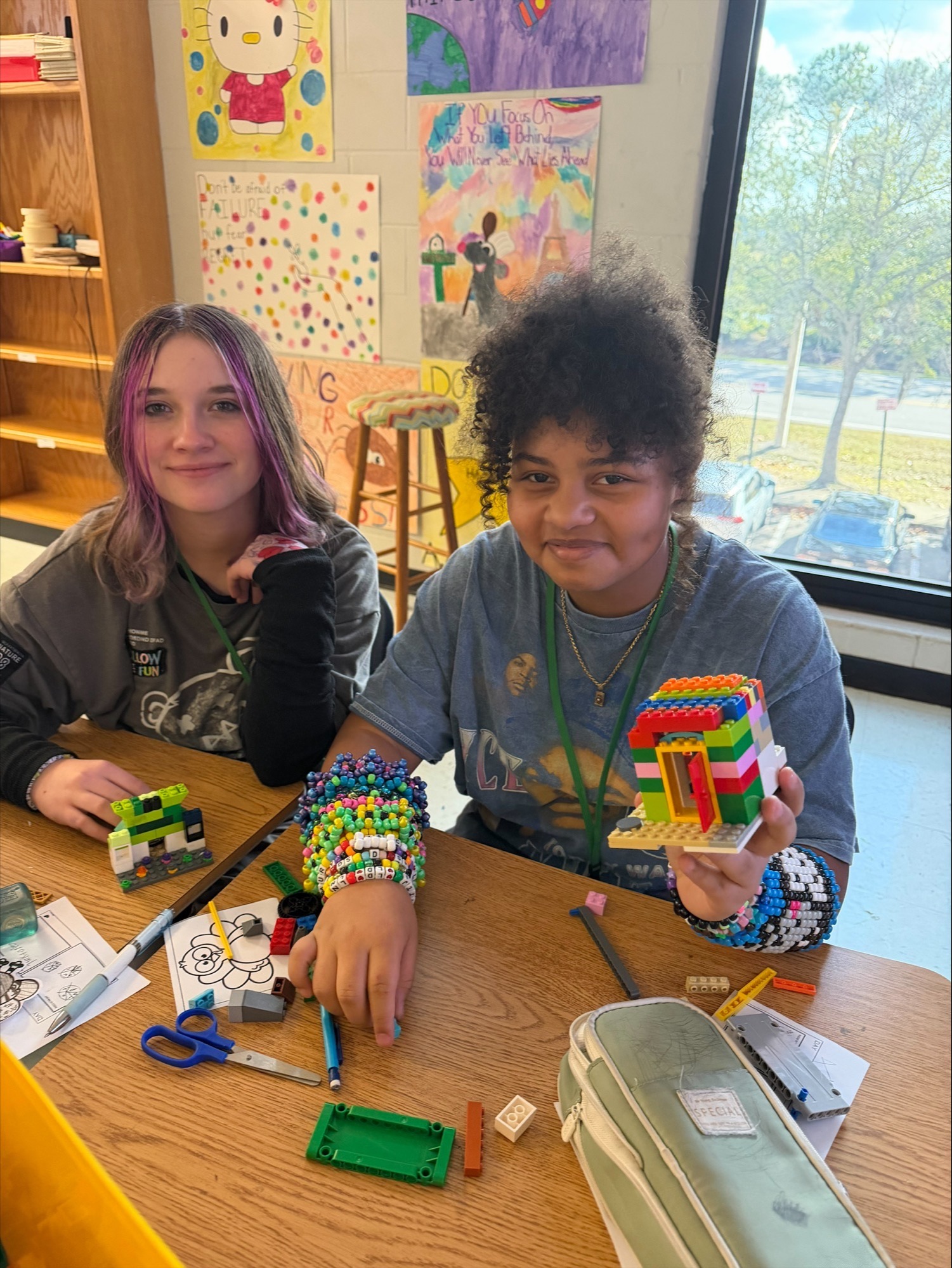 Two female students with protective eyewear.  Both students are wearing back tshirts and jeans.  The students are putting solutions into three test tubes.