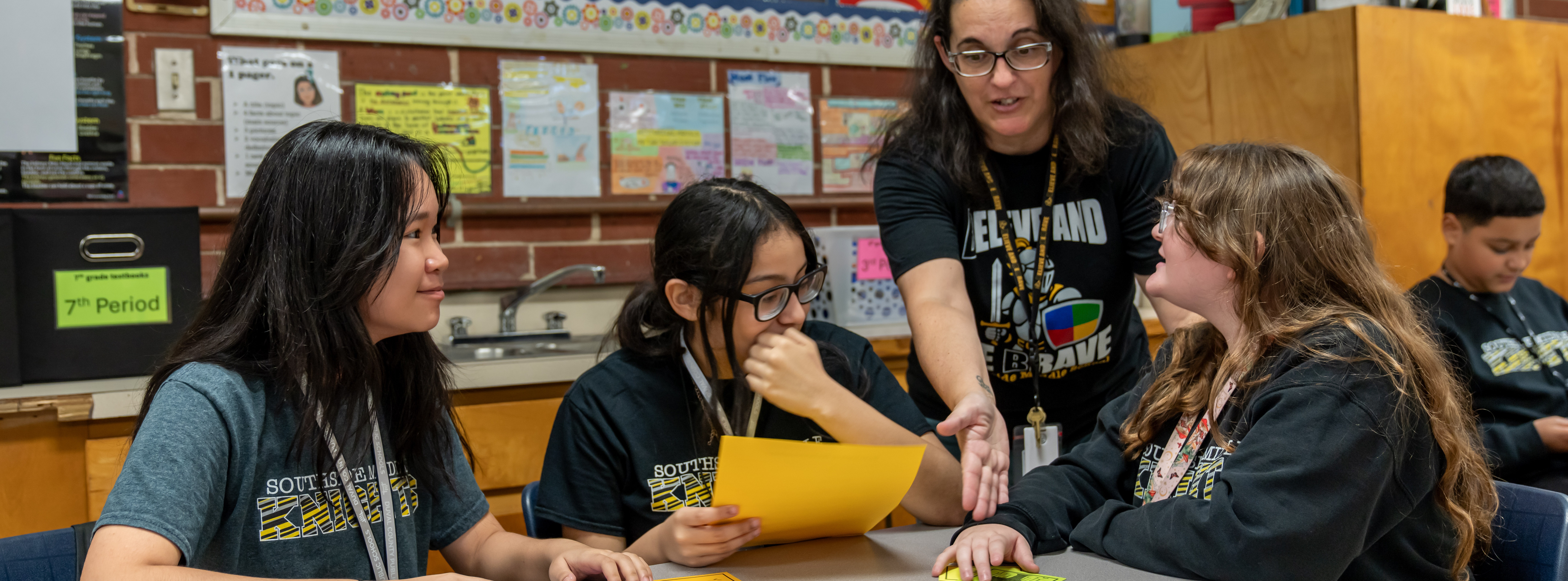 students at a table working on a project with their teacher's help