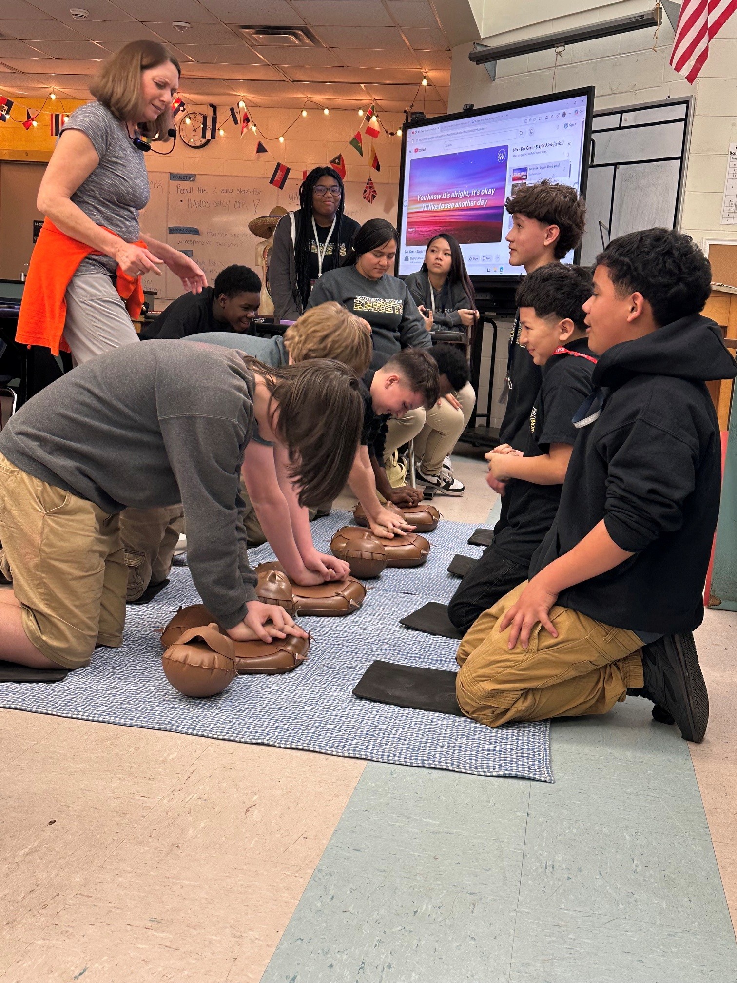 Classroom with a group of students in a circle practicing CPR techniques on manikins with an instructor.