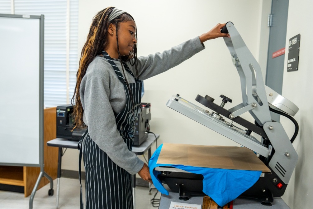 Entrepreneurship student using heat press to apply transfer designed, printed, and made by them.