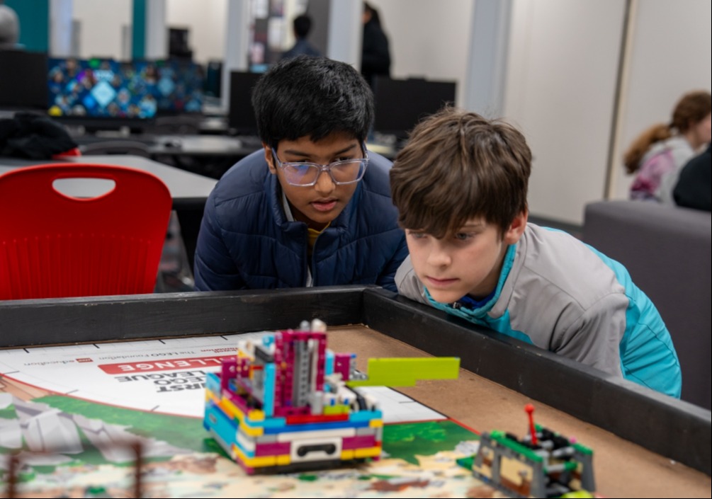 Two students observing a LEGO robot perform a task the programmed it to complete.