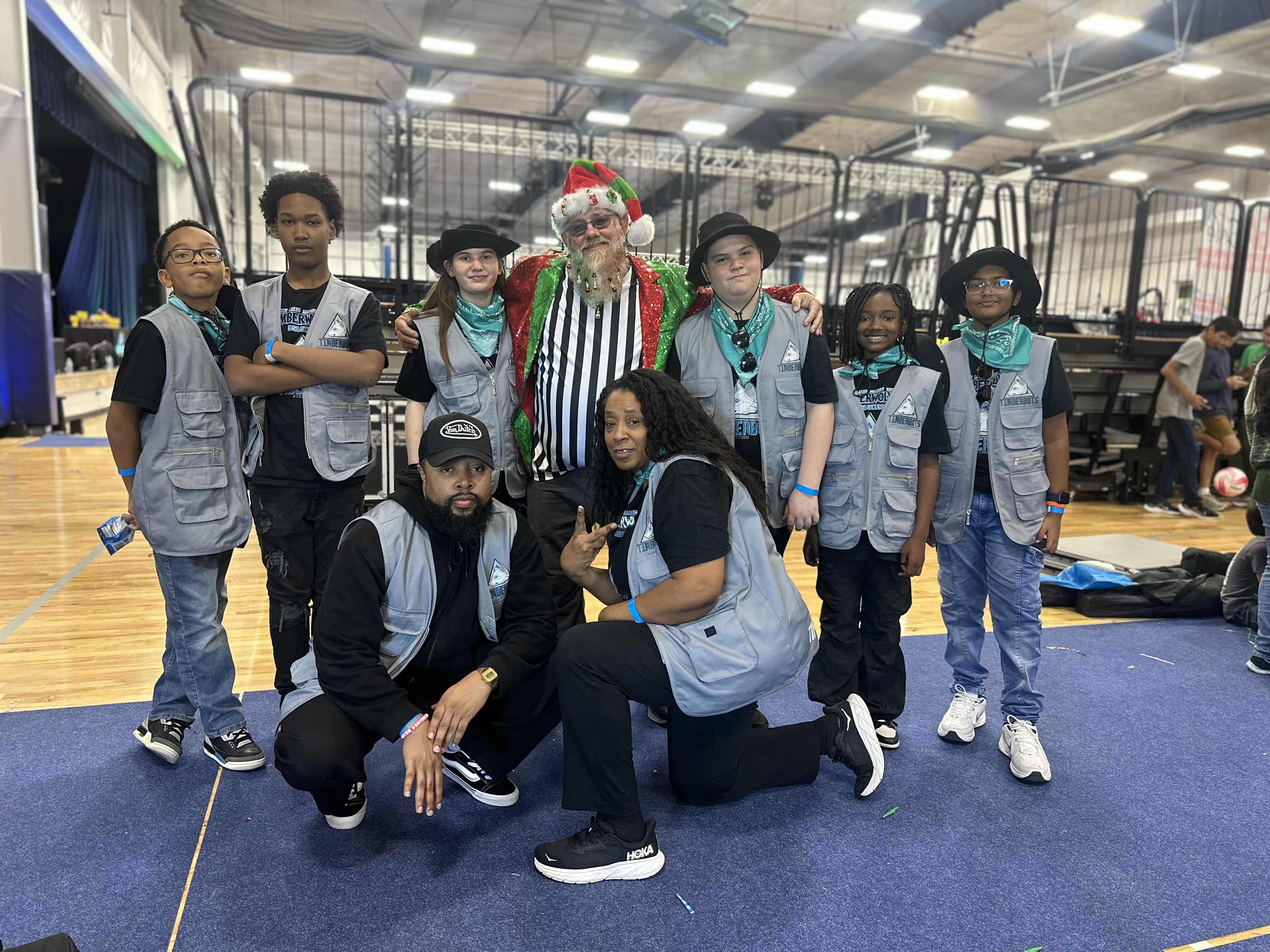 A group of people in vests pose for a photo in a gym with a basketball court.