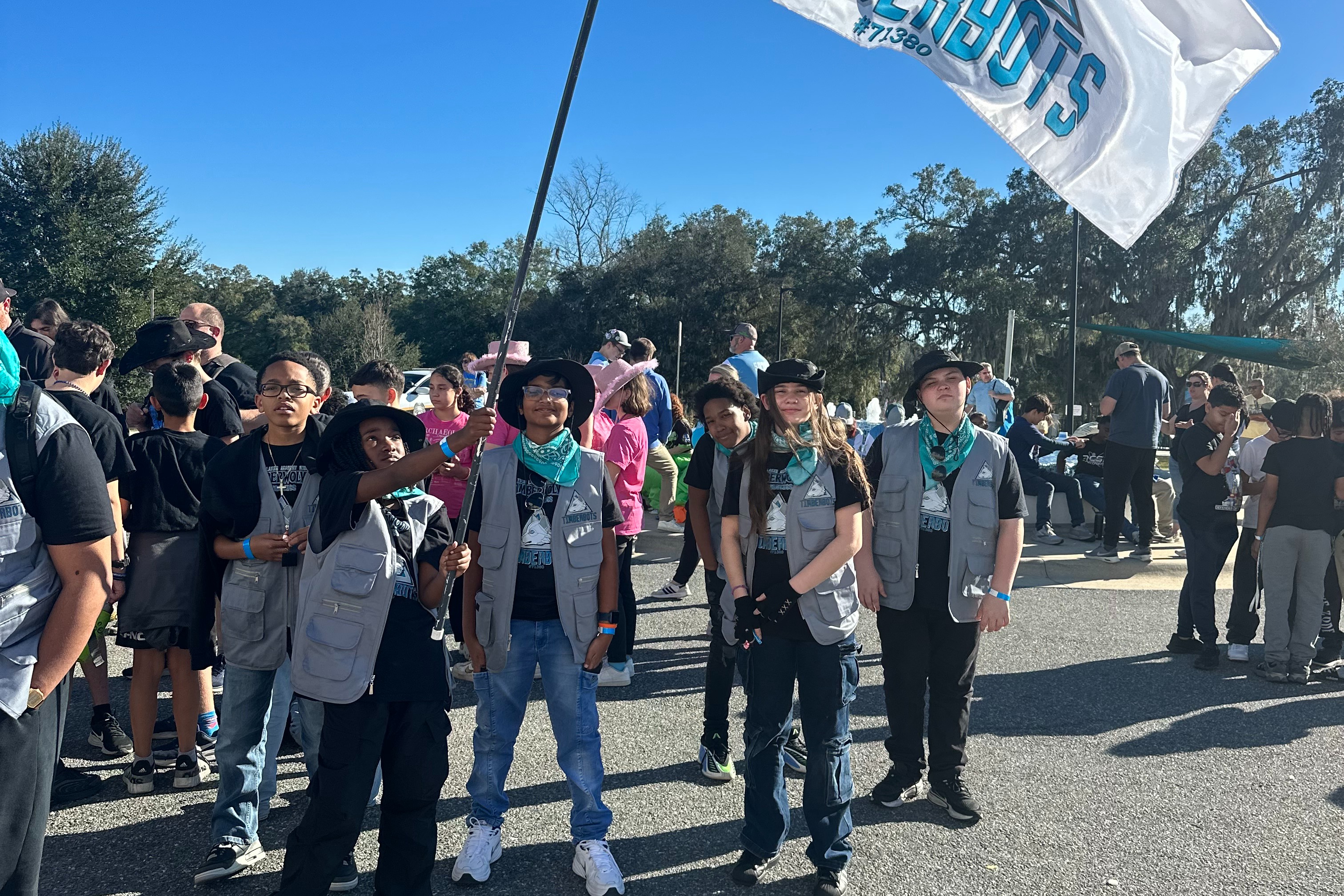 Group of people in vests holding a large flag with text reading "TIMBERWOLVES" in the middle of a road.