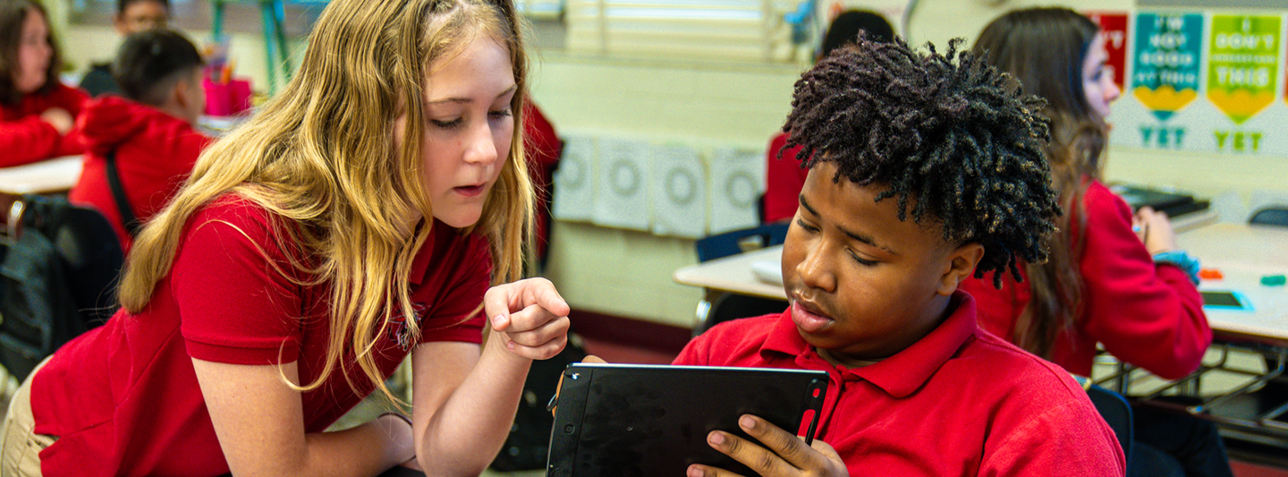 student showing another student something on a classroom tablet