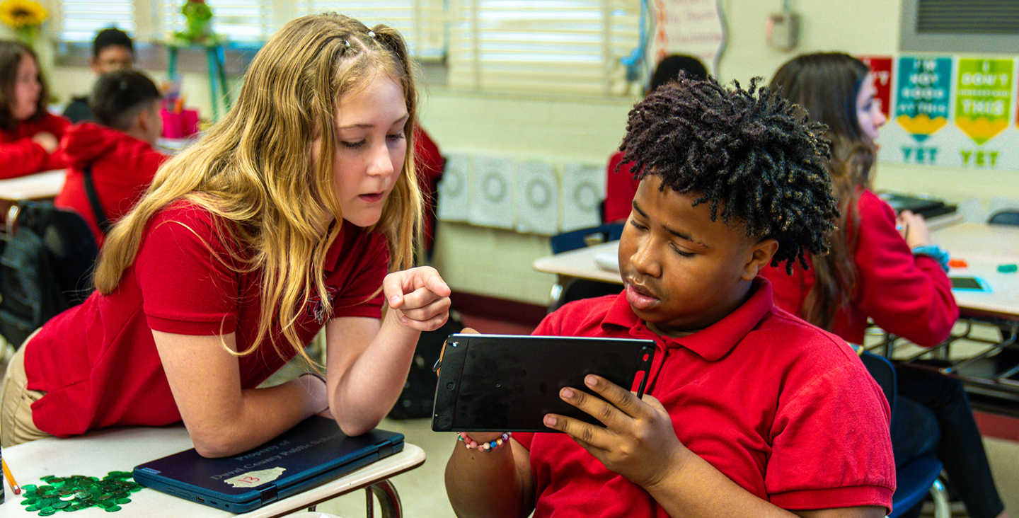 student showing another student something on a classroom tablet