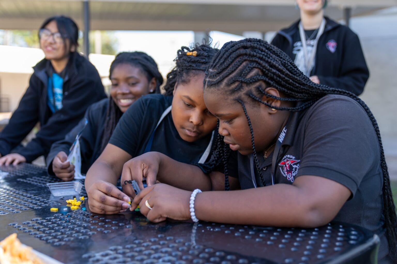 Two students playing with legos, additional students smiling in the background