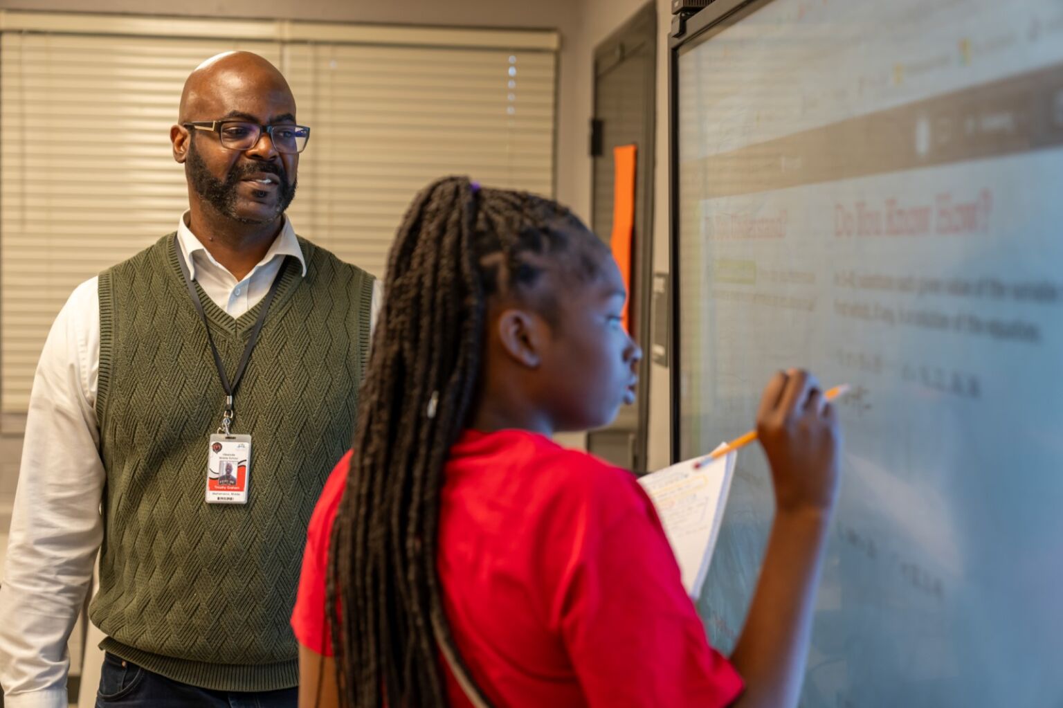 Teacher watching a student do a math problem on the board
