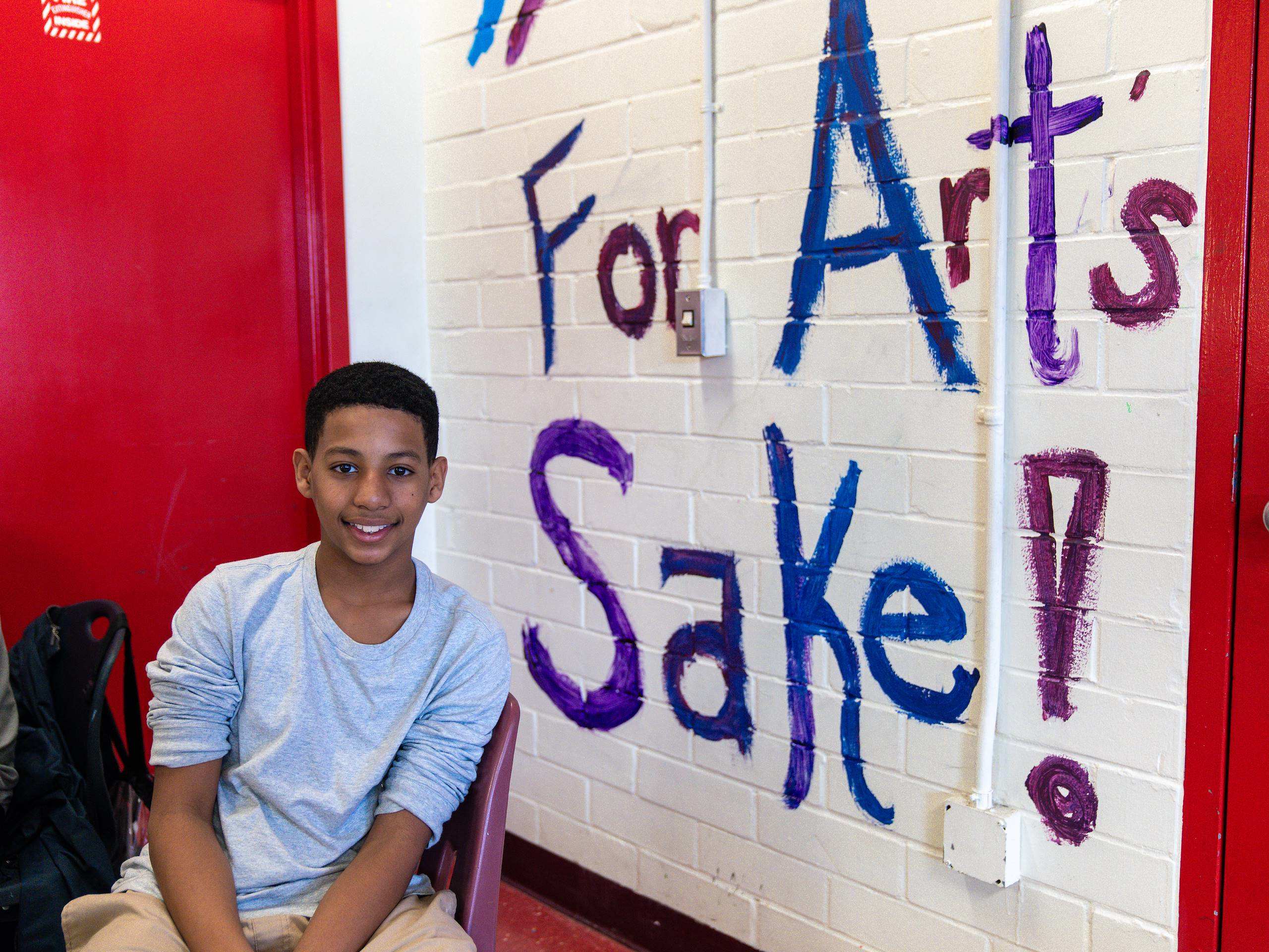 A student smiling next to a wall that says "for arts sake"