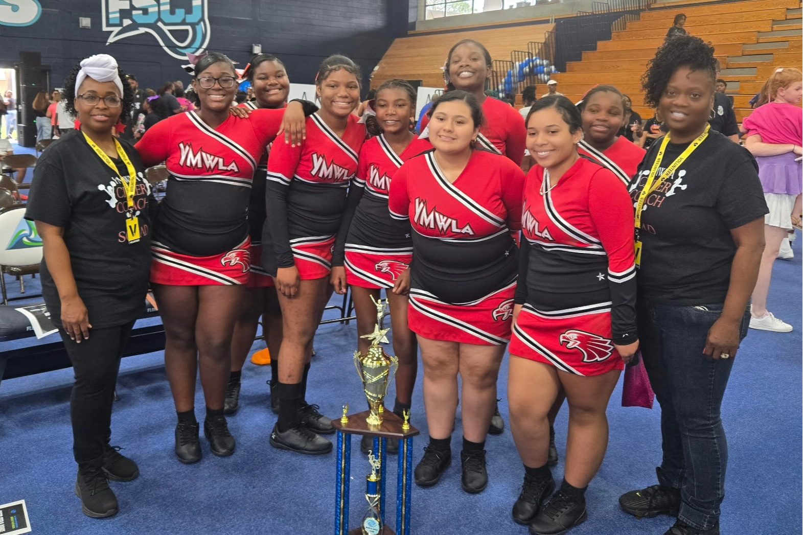 YMWLA Cheer coaches and squad smiling for a photo after winning a large trophy at the FSCJ Cheer competition 2025