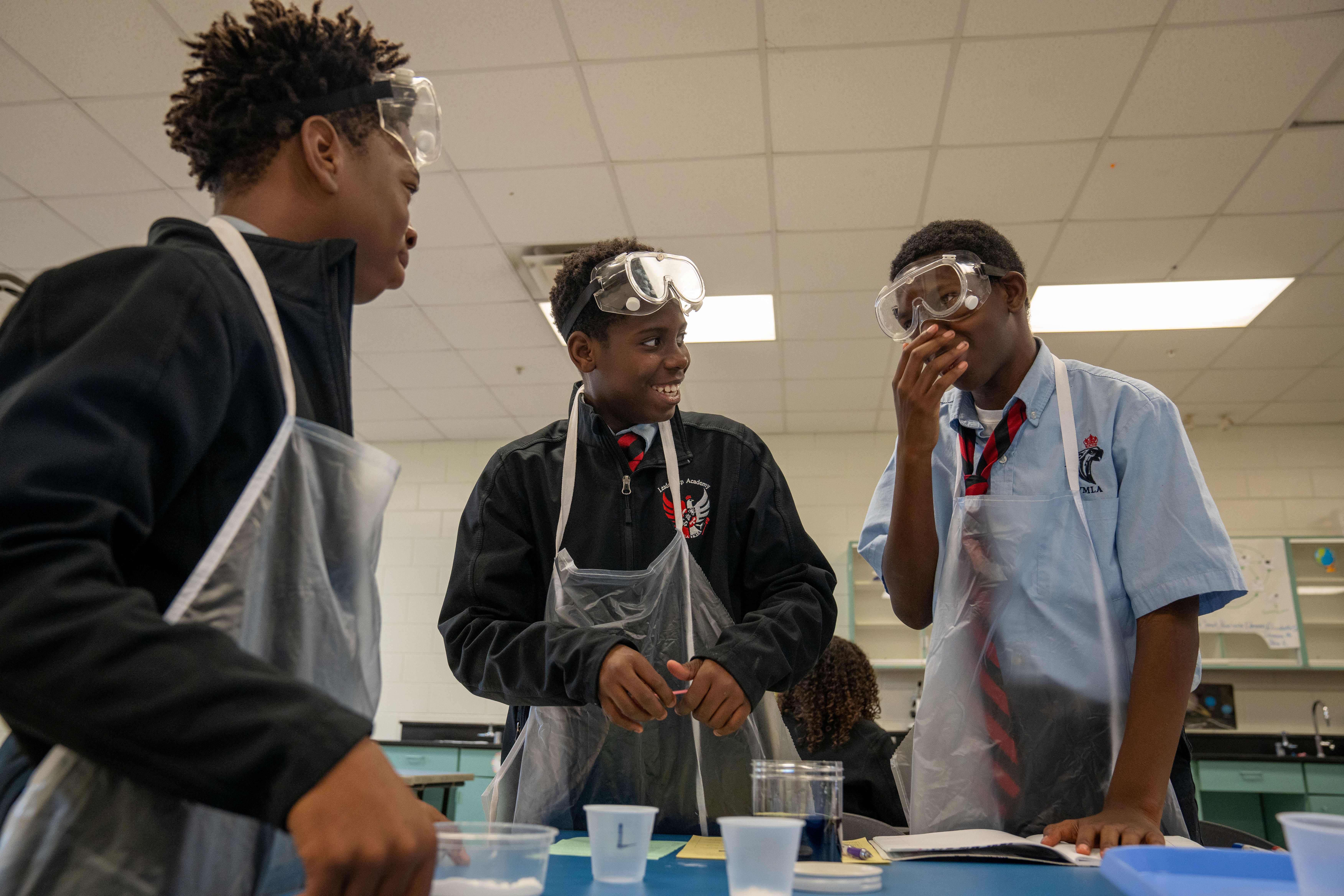 3 students working together and having fun, smiling, and laughing while completing a science experiment