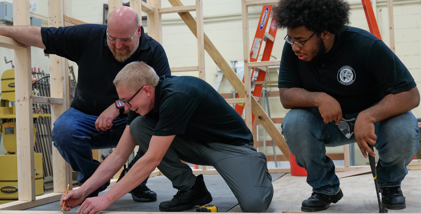 Students working on a wood frame with their teacher. 