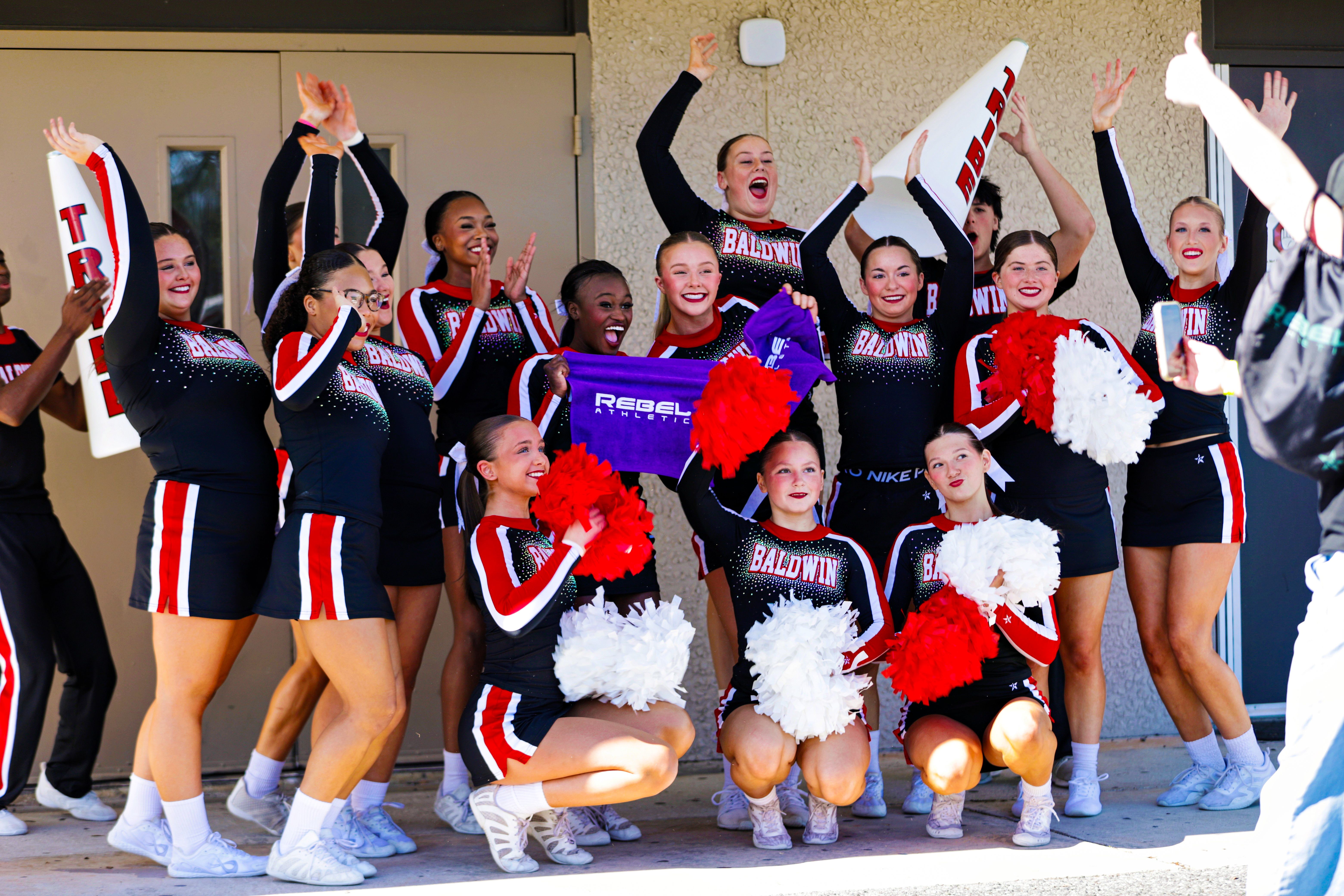 Cheerleaders in black, red, and white uniforms pose for a photo outside a building.