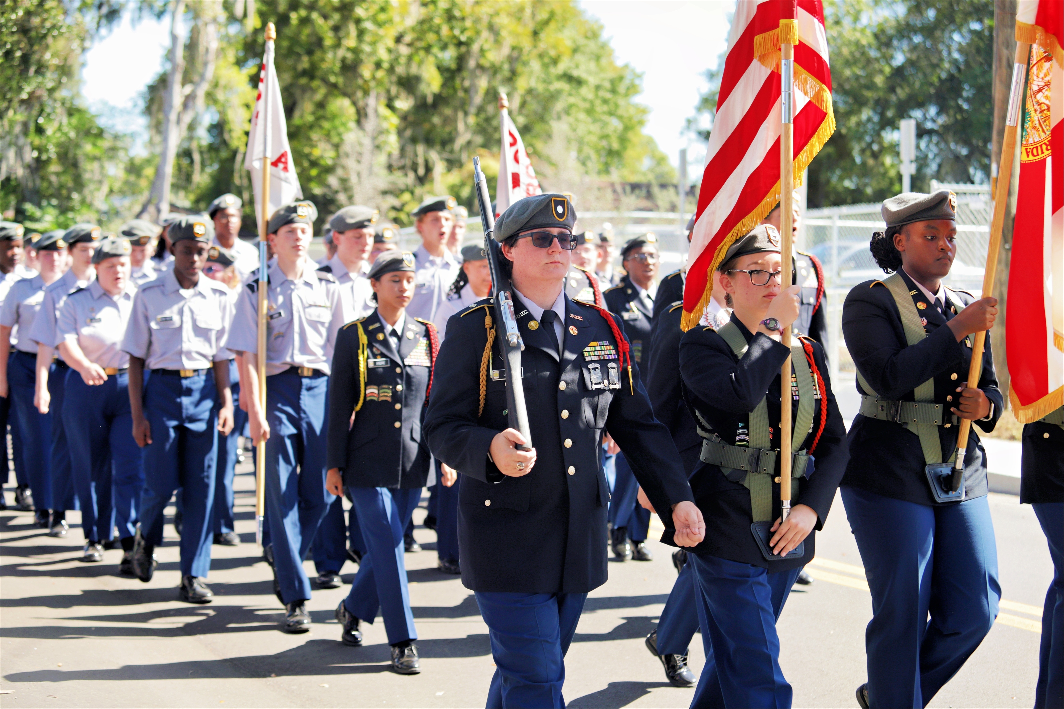 A group of uniformed individuals, holding flags, marching in a parade on a street.