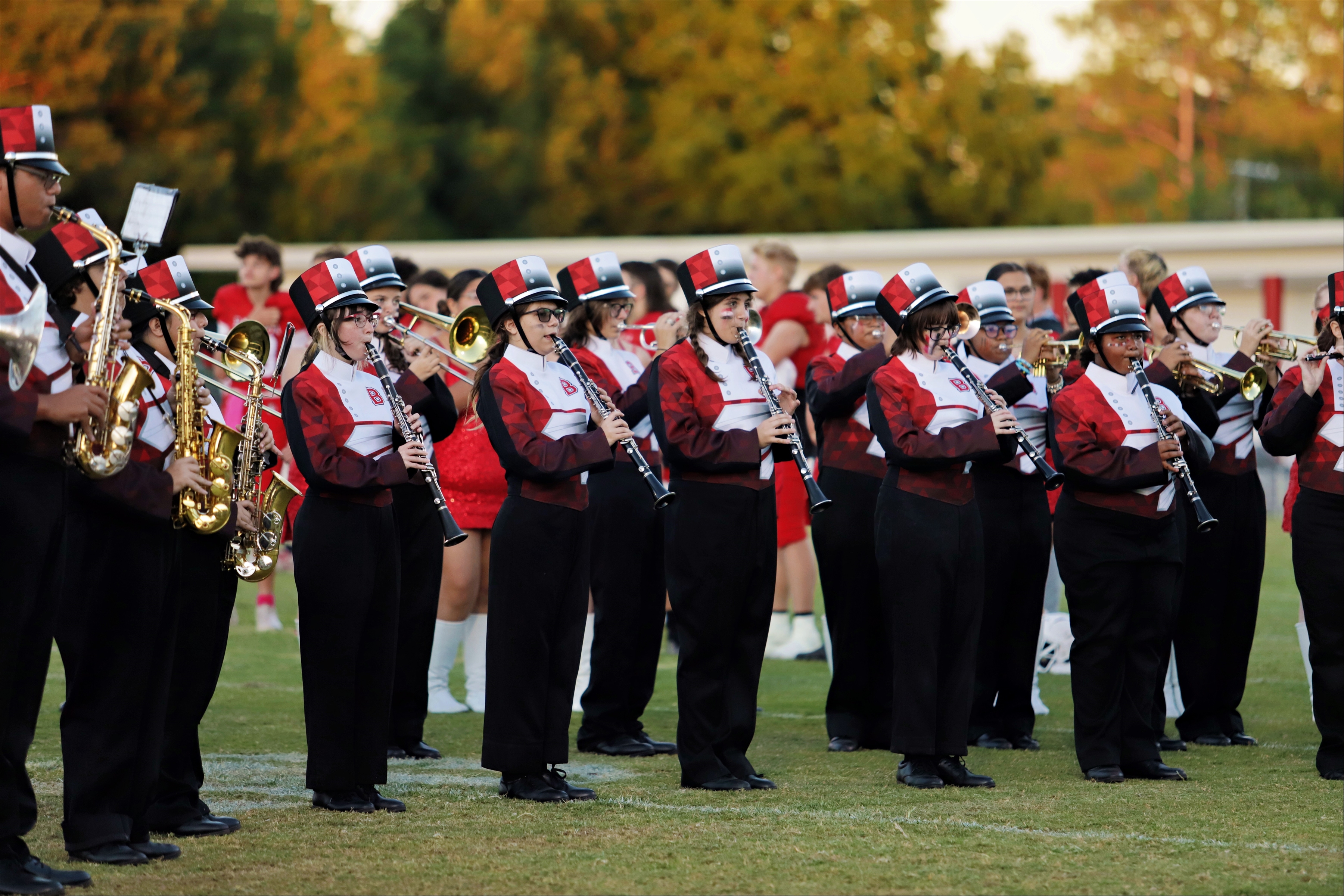 A school band in red, white, and black uniforms stands on a field, holding musical instruments.