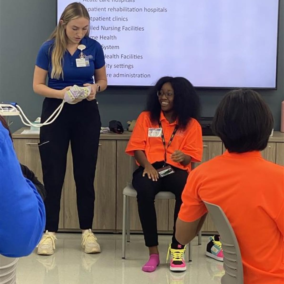 A woman demonstrates a skill in front of a group of three. A screen in the background shows the heading "Where can we work?"