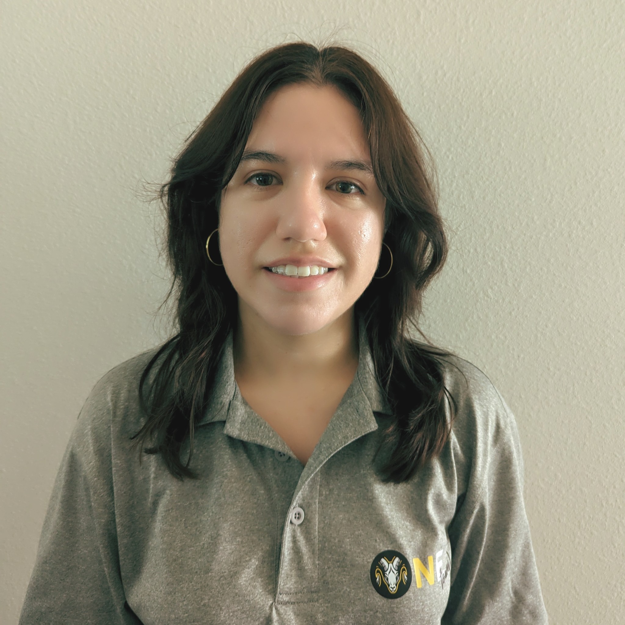 A woman with dark brown hair wearing a gray polo shirt with a logo on the left chest area.