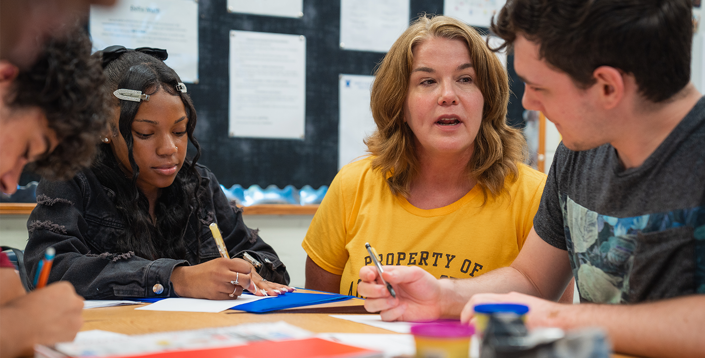 students at a table with teacher working on class assignments