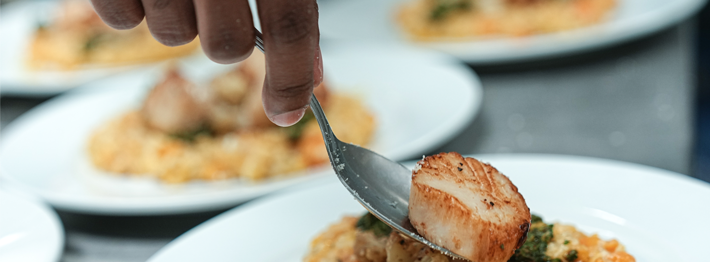 plate of risotto with a seared scallop being placed on top