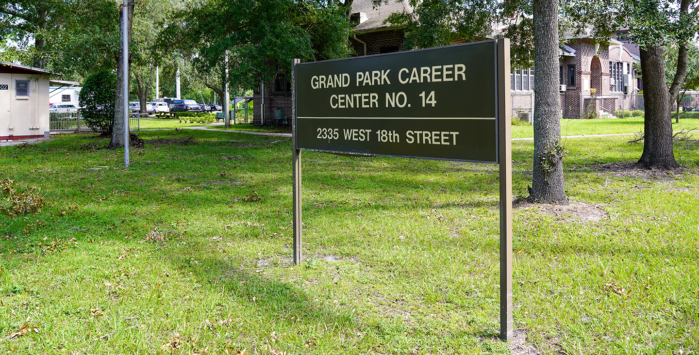 Green sign in grass "Grand Park Career Center No. 14, 2335 West 18th Street"