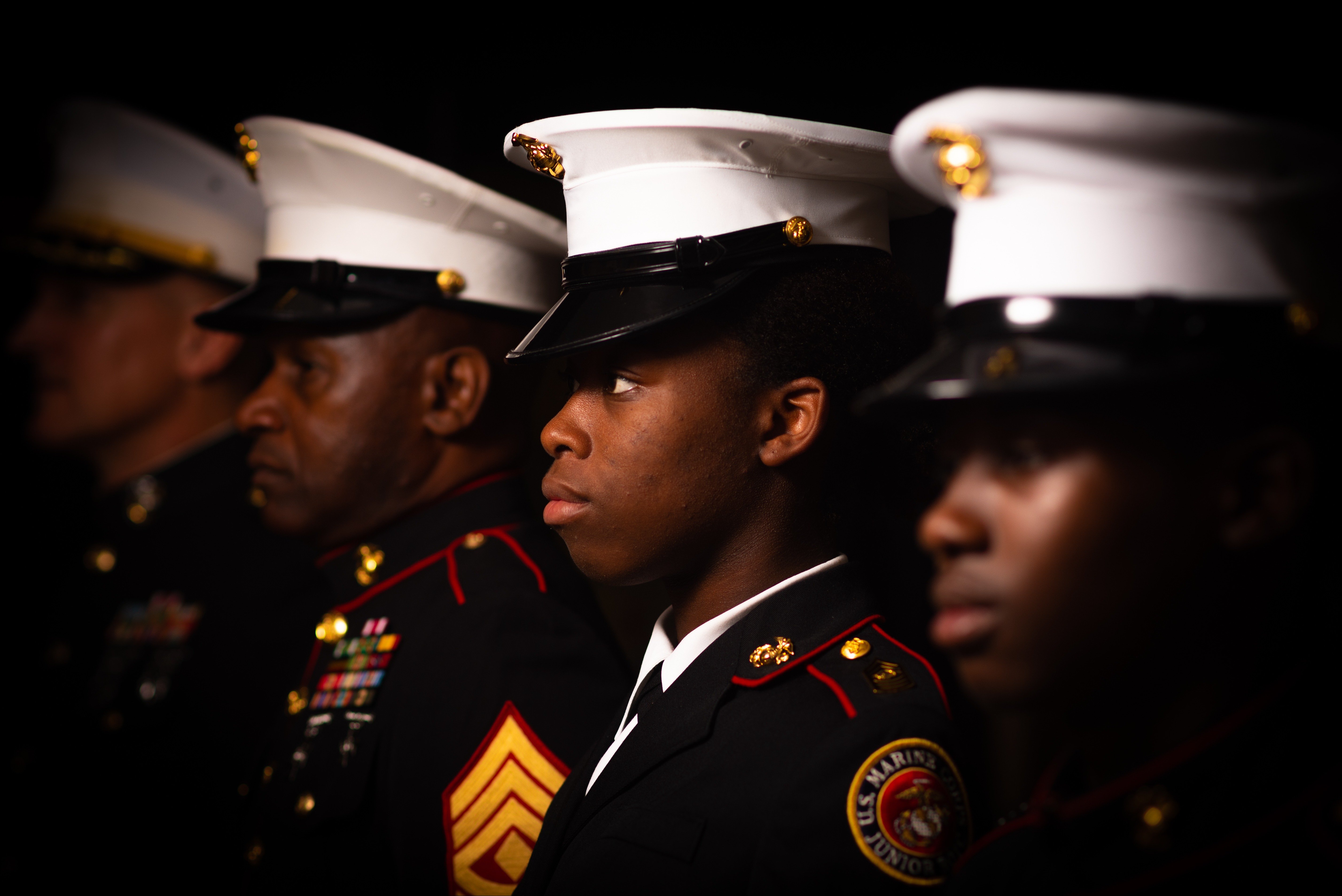 Five military personnel in uniform, standing side by side in a row, facing the same direction.