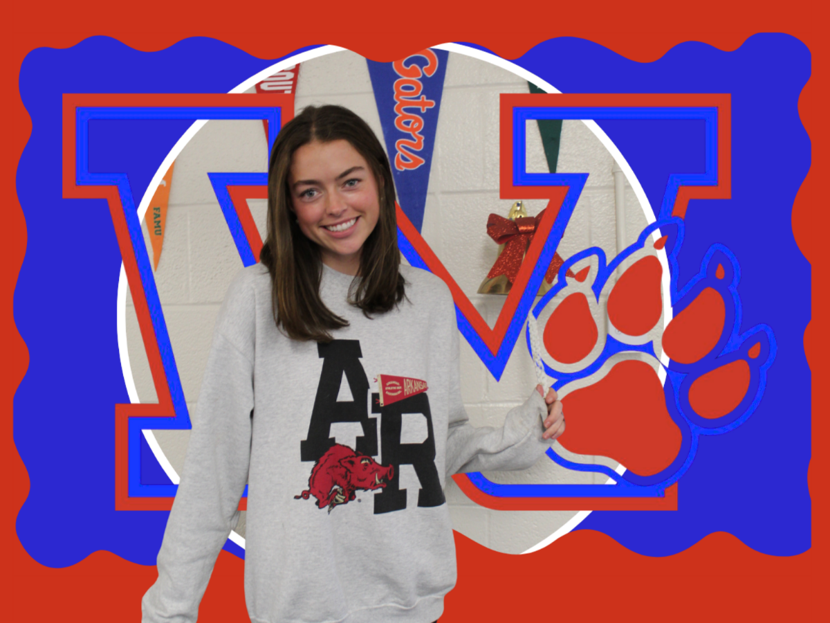 A young woman stands in front of a school logo. She wears a gray sweatshirt with "AR" and a red paw print.