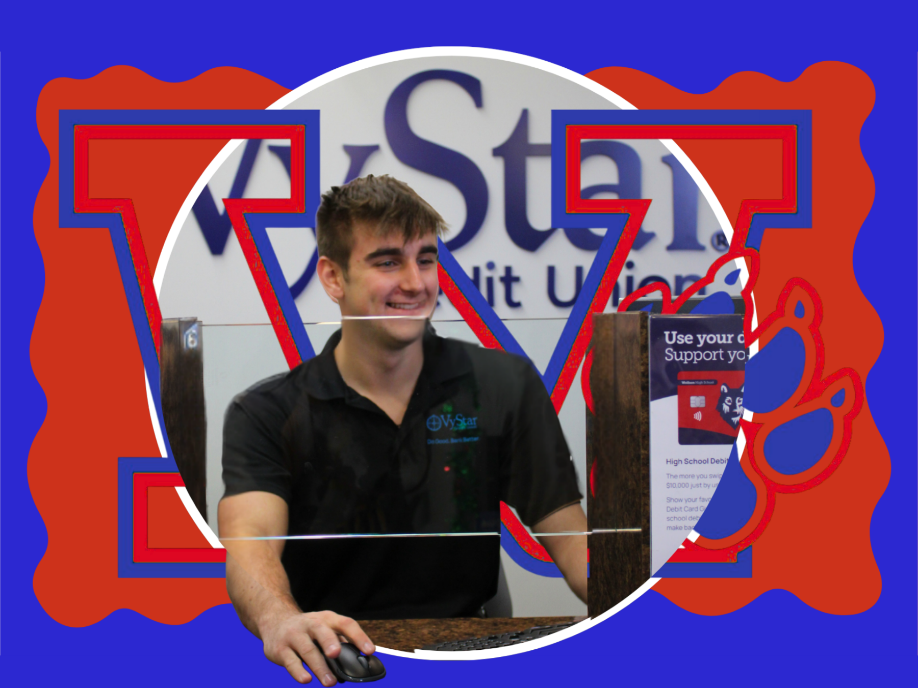 Man in a black shirt smiles and holds a mouse while sitting in front of a computer.