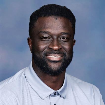 Person in white collared shirt with logo on left chest area. Wearing black collar and buttons. Smiling.