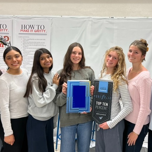 A group of eight women stand together holding a box with blue cover in front of a white backdrop.