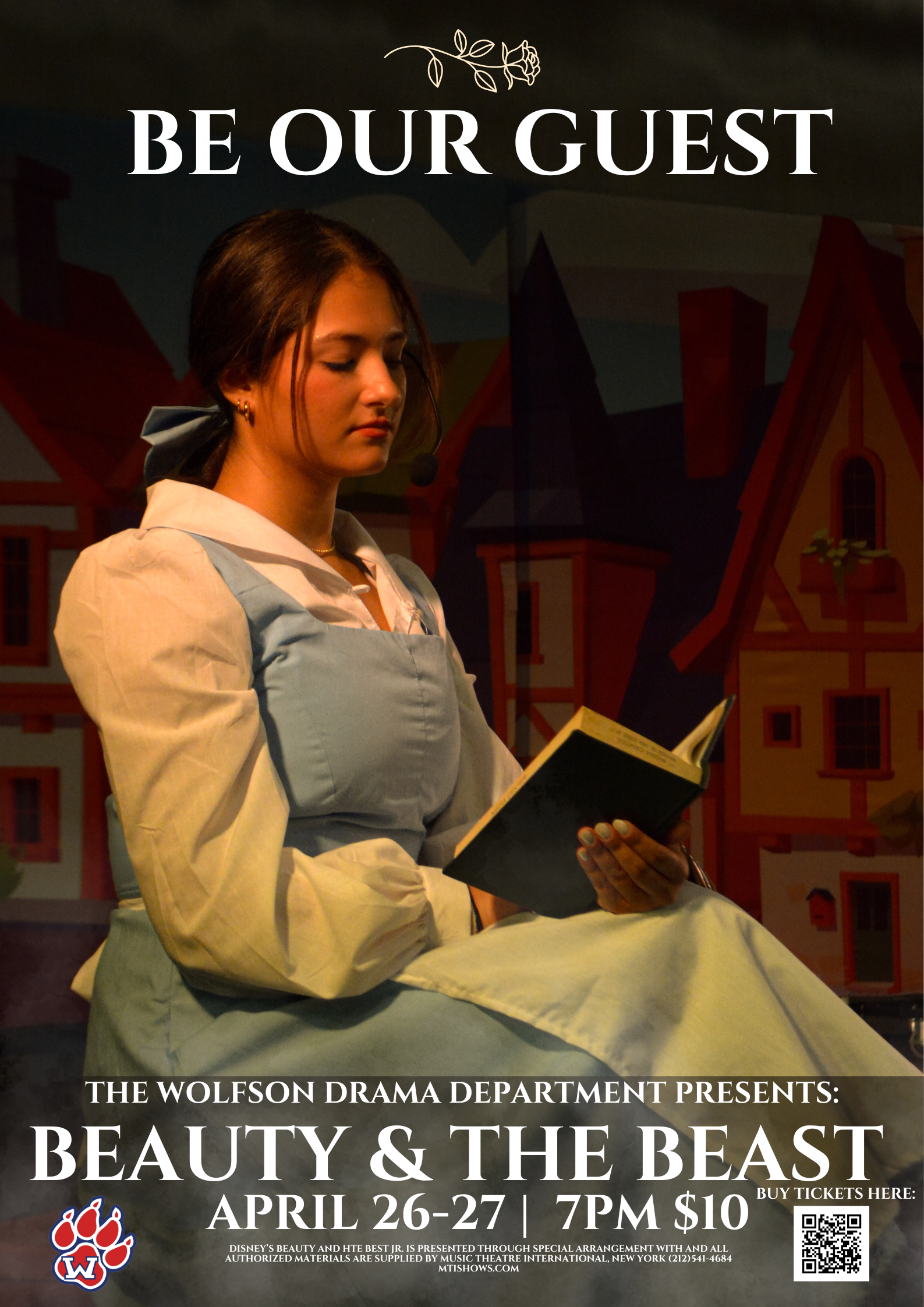 A woman in a blue dress sits and reads a book in front of a colorful building backdrop.