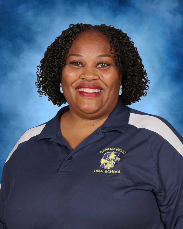 Woman with curly hair, smiling, wearing a blue and white polo with a logo on the left chest.