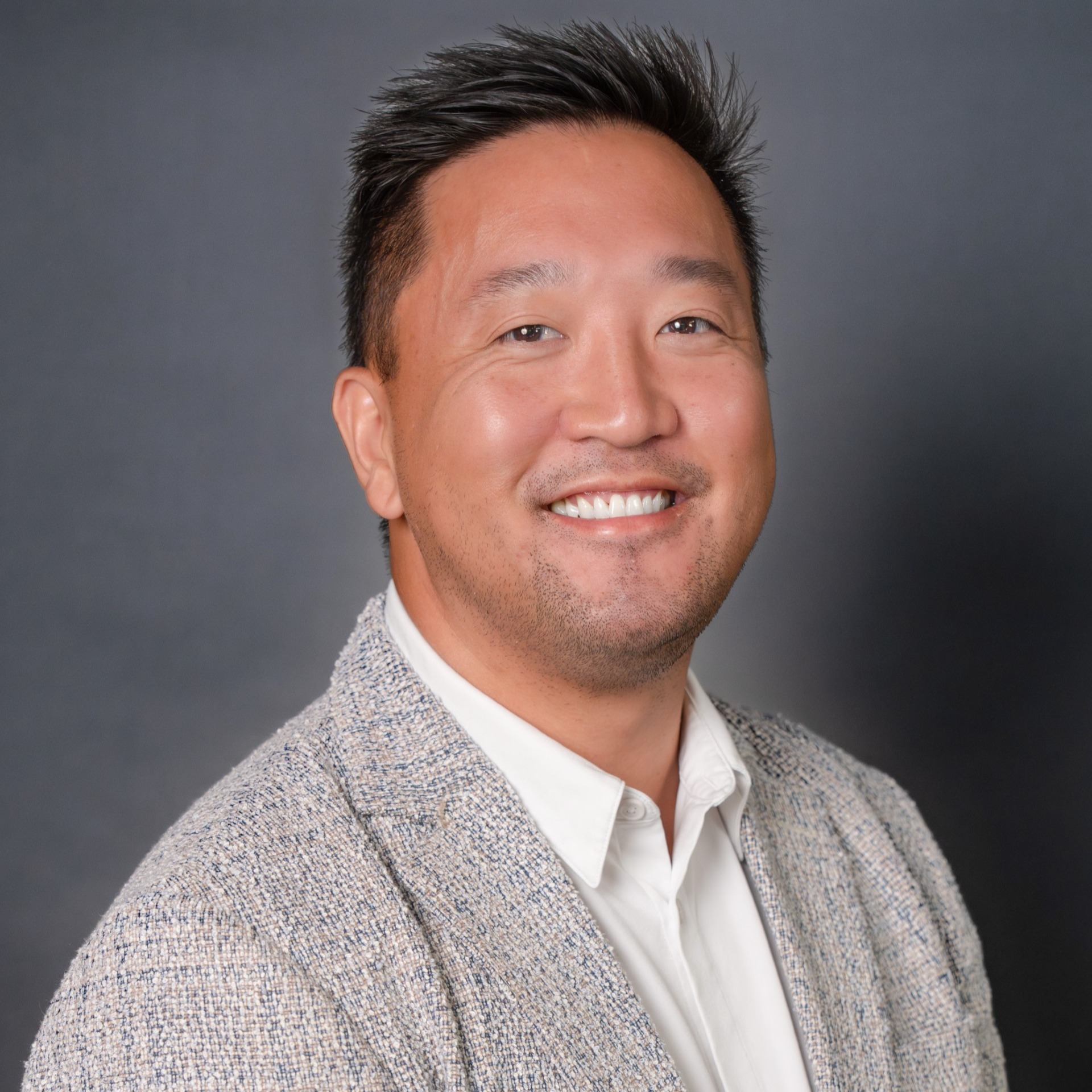 A smiling man in a gray blazer over a white shirt poses against a gray background.