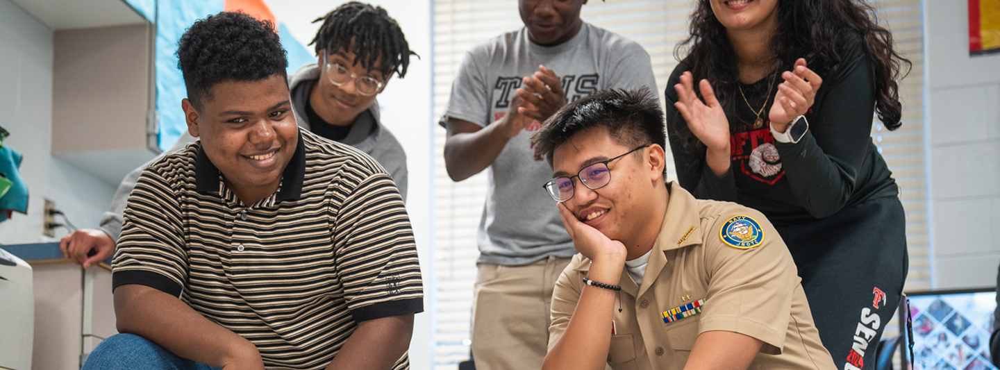 Students clapping and squatting to pose for the camera in a classroom