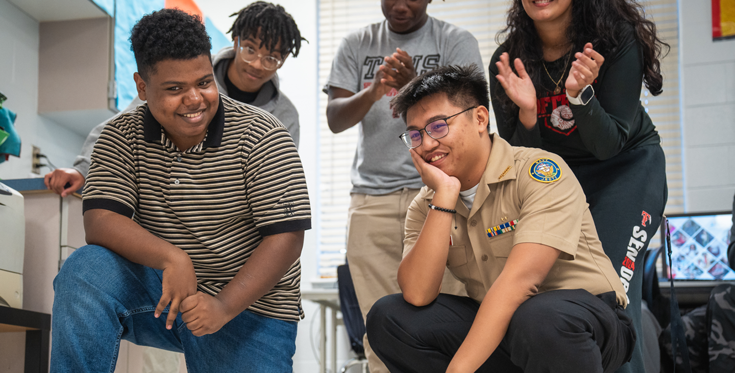 Students clapping and squatting to pose for the camera in a classroom