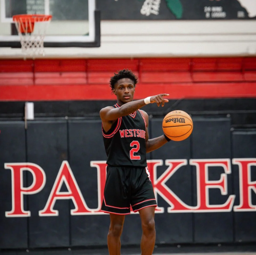 Basketball player in jersey number 2 holding ball, standing in front of a wall with "Paiker" in large red letters.