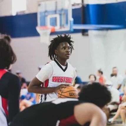 A basketball player with short, curly hair holding a basketball in an indoor sports facility.