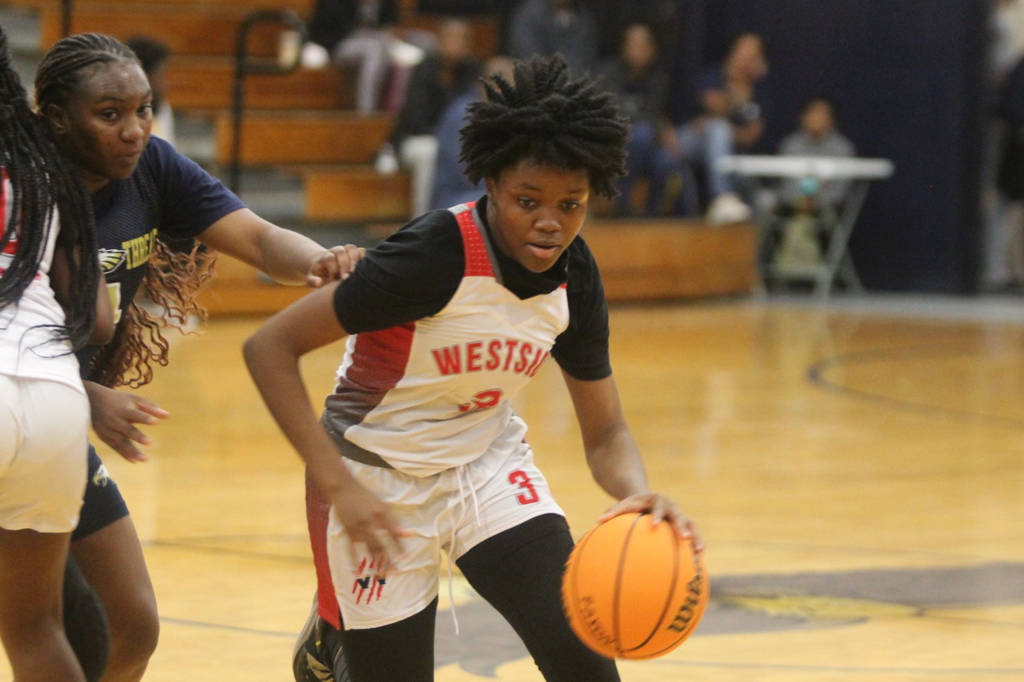 Three girls playing basketball on a court. One girl is dribbling while two others attempt to block.