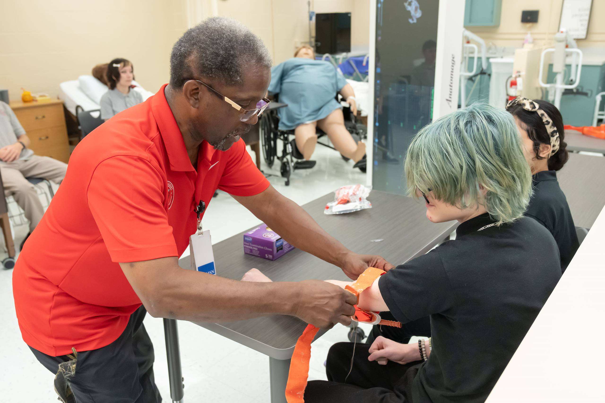 Man in red shirt helping seated woman with blue hair adjust a blood pressure cuff on her arm.