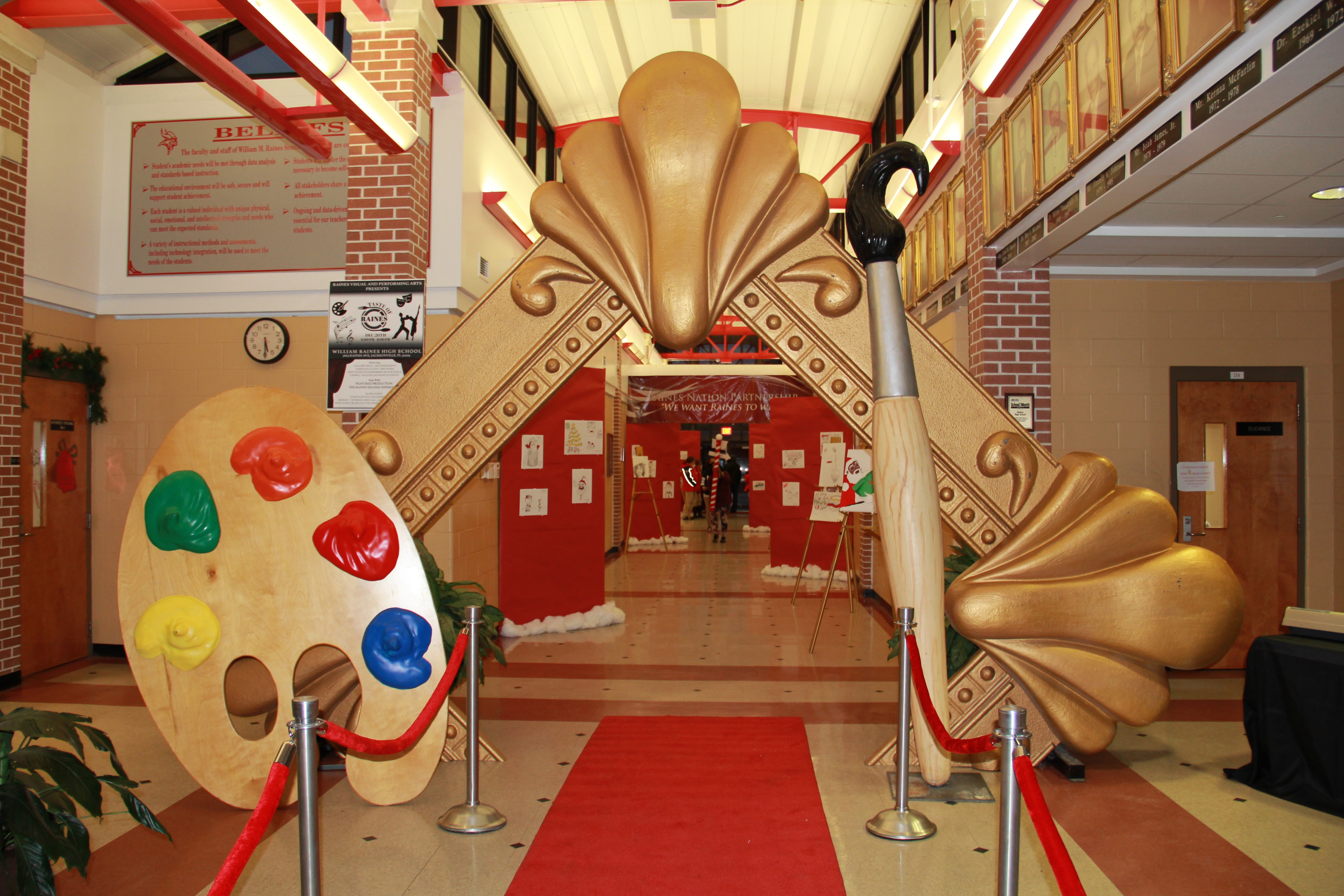 Interior hallway with large gold paint palette and brush arch over a red carpet leading to a door.